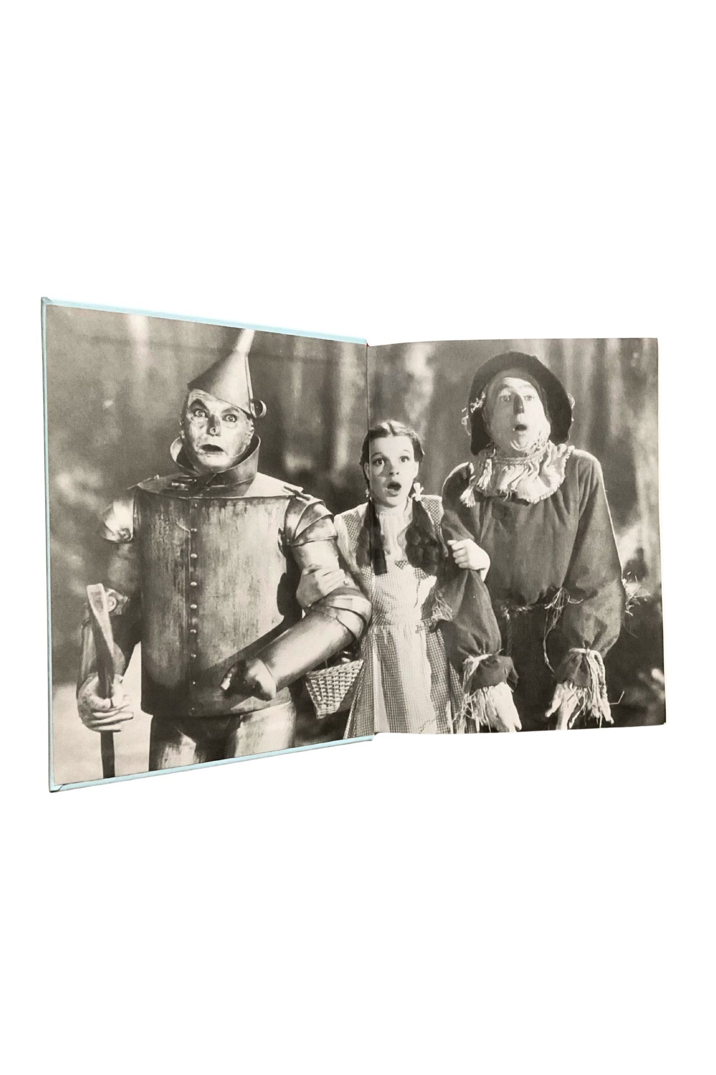 Open book showing vintage black and white photo of characters from 'The Wizard of Oz' on a white background