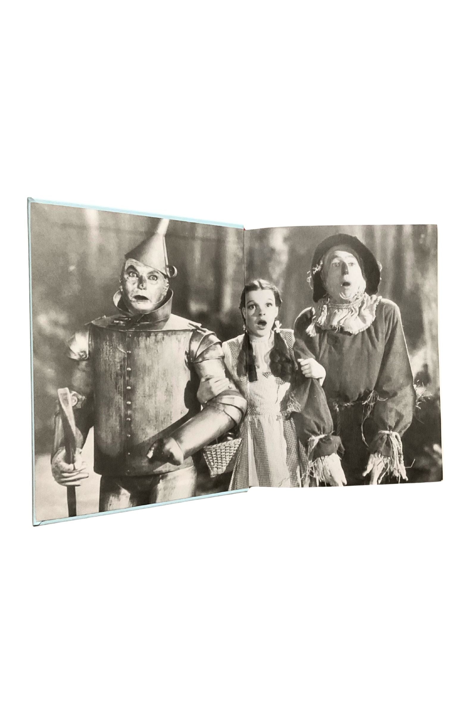 Open book showing vintage black and white photo of characters from 'The Wizard of Oz' on a white background